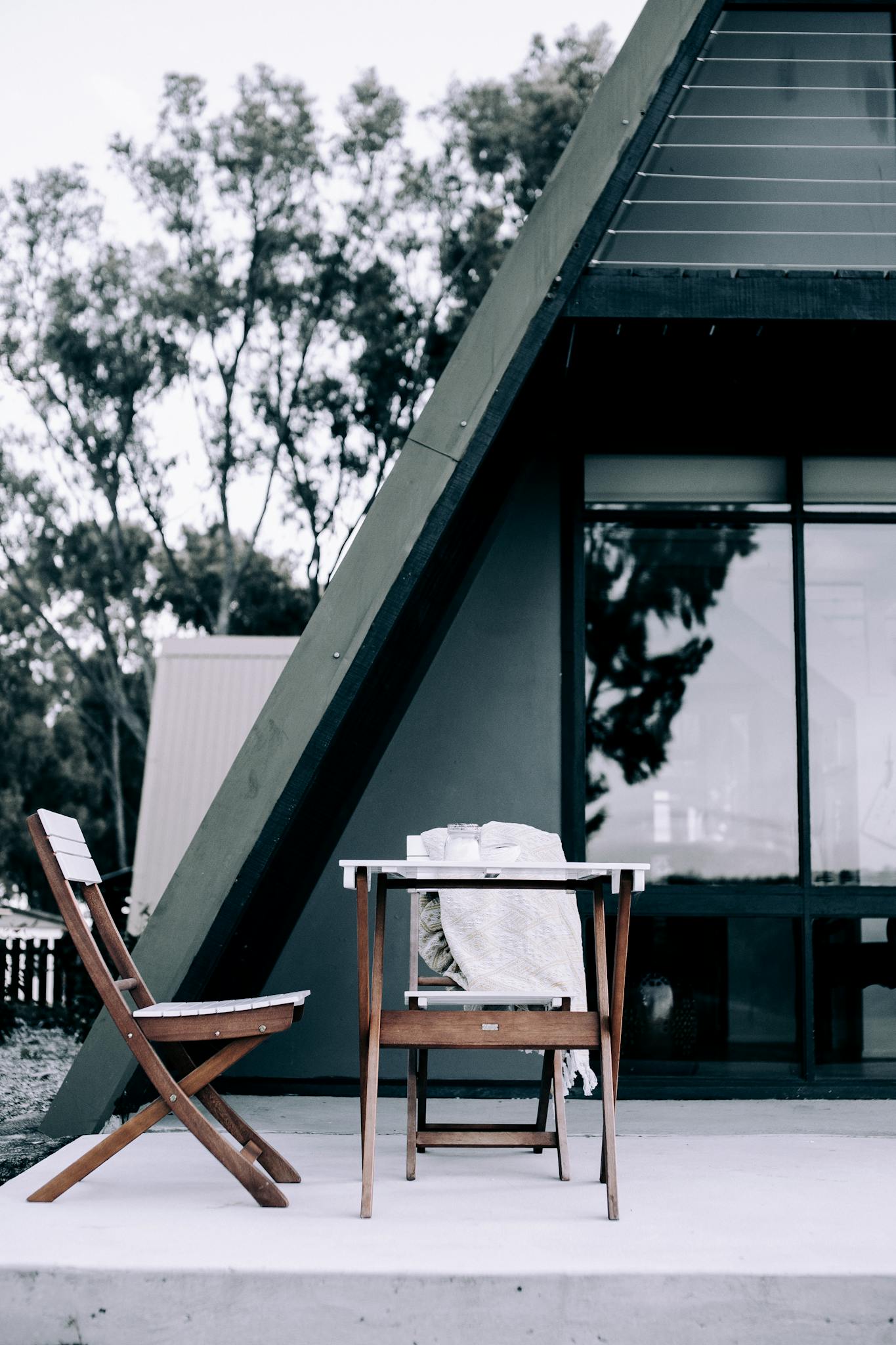 A serene patio with wooden chairs and table by a modern A-frame cabin.