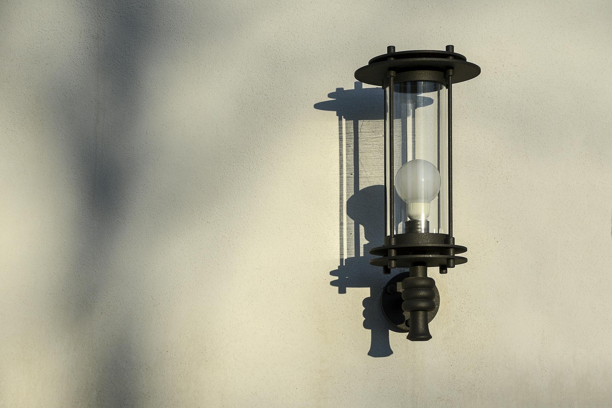 Elegant outdoor wall light casting shadow on textured wall in sunlight.
