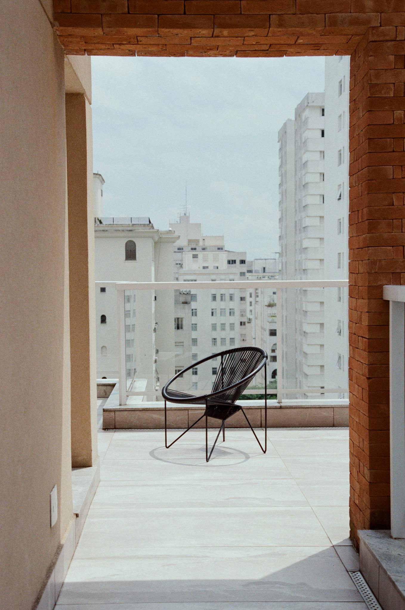 Minimalist balcony with chair and cityscape view on a sunny day.